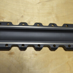 "Metal gasket or sealing component with multiple bolt holes, designed for industrial machinery or automotive applications, displayed on a wooden surface."