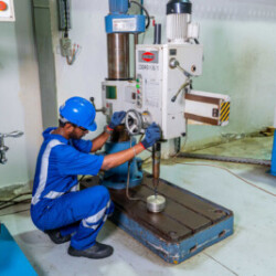 Technician operating a radial drilling machine for precision drilling in a workshop.