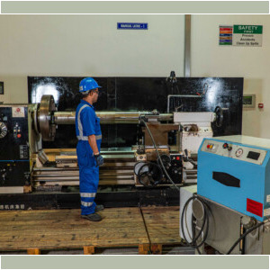 Technician operating a lathe machine in an industrial workshop with safety gear.