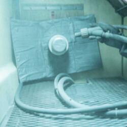 Industrial sandblasting or cleaning chamber with hoses and a metal component secured for surface treatment or preparation.