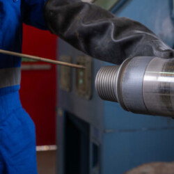 Technician wearing protective gloves and overalls inspecting a cylindrical metal component