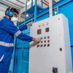 Technician wearing protective gear operating an industrial control panel in a factory setting