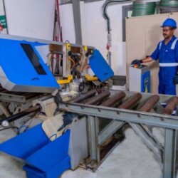 "Technician operating an industrial metal cutting bandsaw in a workshop."