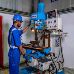Technician operating a vertical milling machine in an industrial workshop.