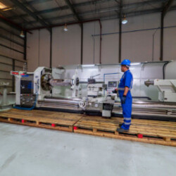 Technician operating a large industrial lathe machine in a spacious workshop